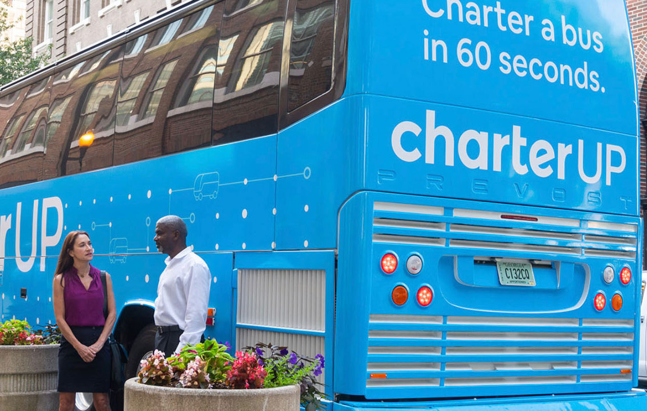 two people stand and talk in front of a blue CharterUP bus
