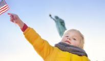 A young New York City child student stands in front of the Statue of Liberty