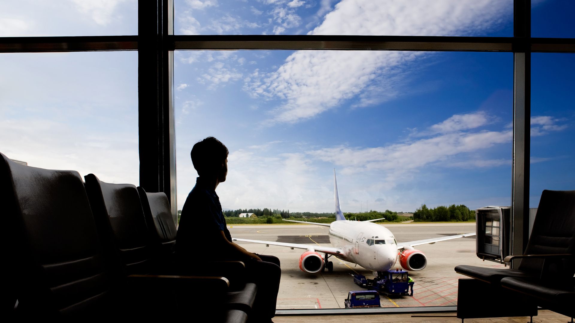 A passenger at the airport looks out the window at an airplane on the tarmac