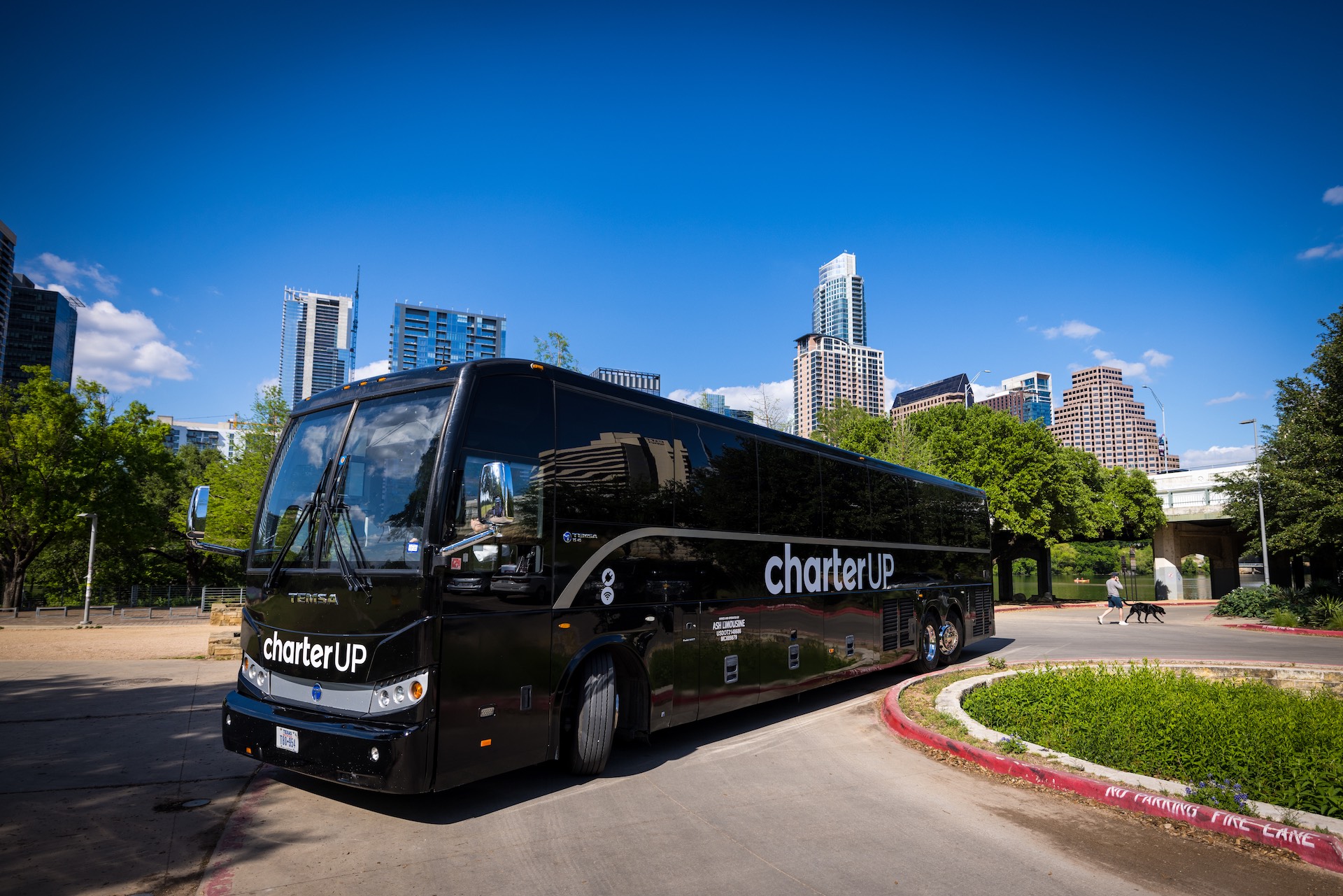 A black luxury coach with CharterUP branding parks in front of the Austin skyline