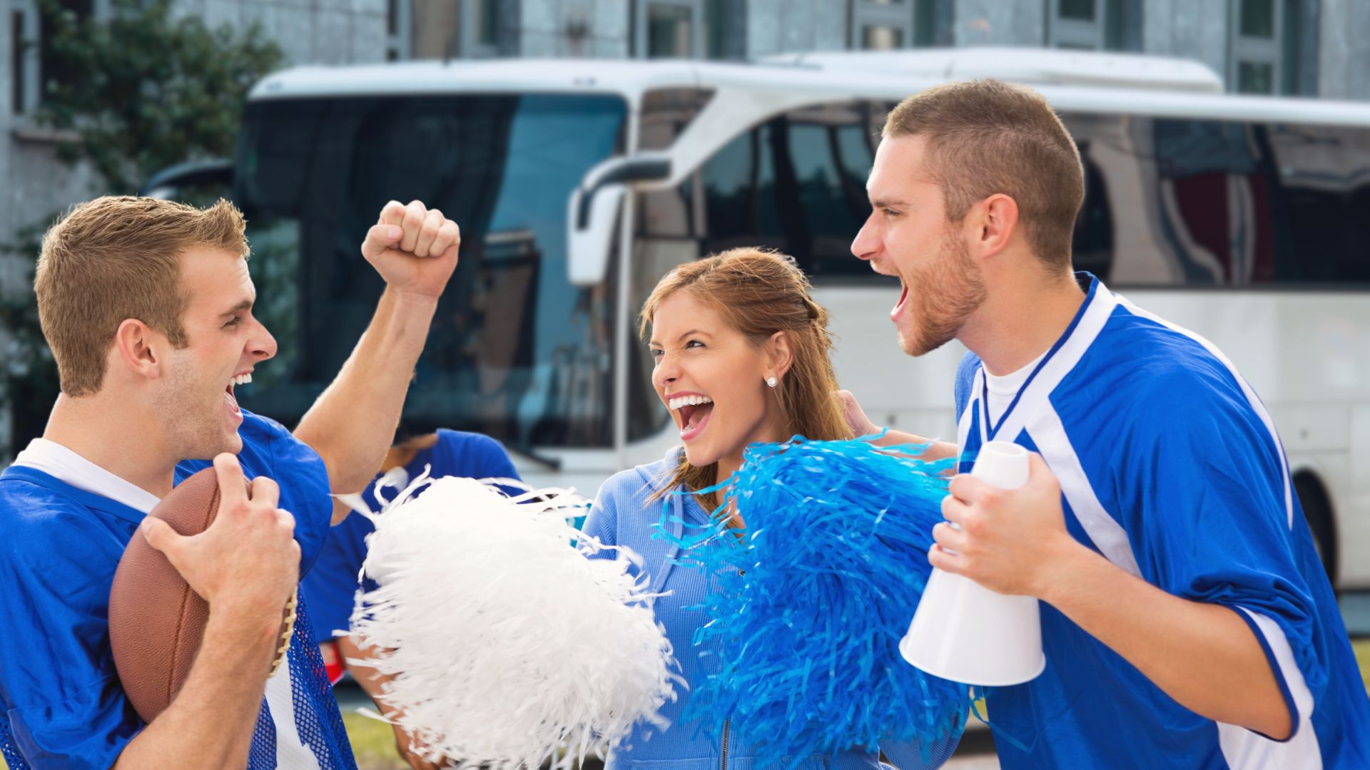 Sports fans dressed in spirit gear cheer in front of a charter bus