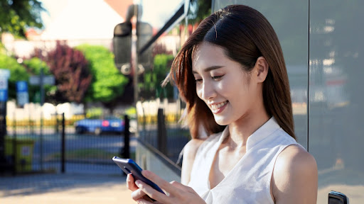 A woman smiles as she looks at her phone while standing in front of a charter bus