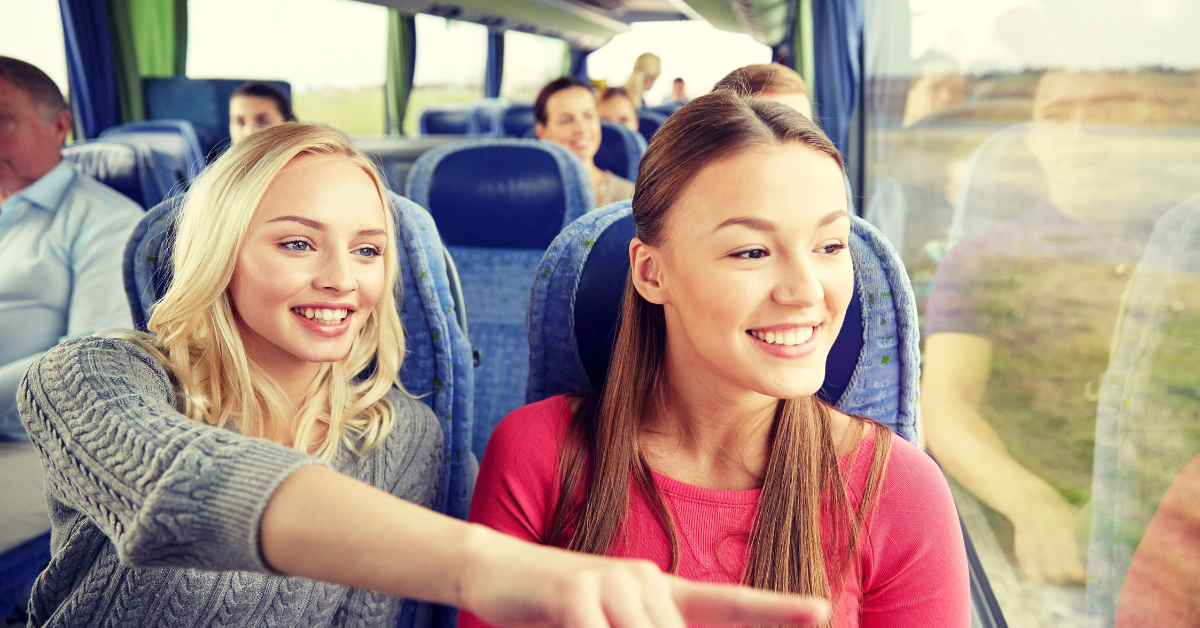 Two women excitingly looking out the window on a charter bus